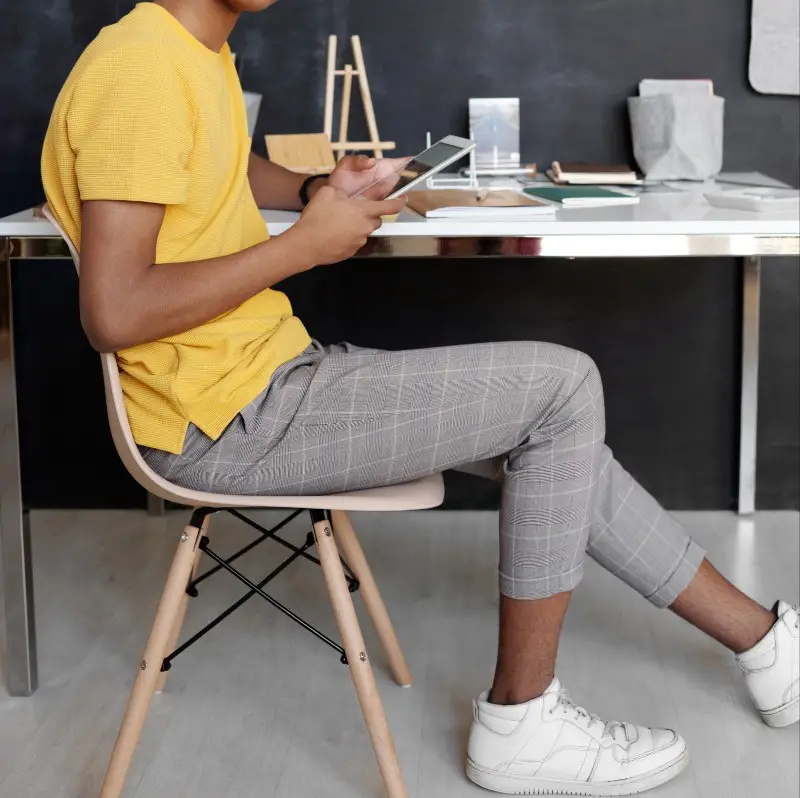 A teen guy sitting on a chair, holding mobile in his hand.