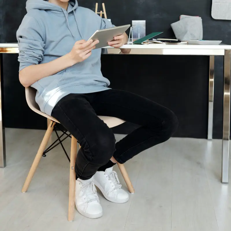 A teenage guy sitting on a chair, operating mobile phone.