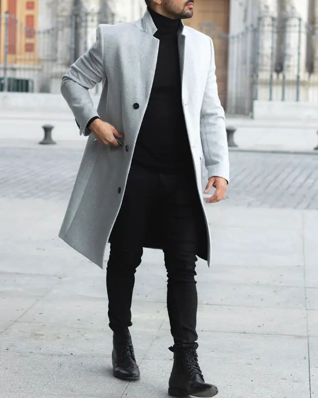 A man in long coat, high neck, Chelsea boots and slim fit jeans.