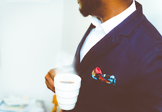 A man in navy blue suit, coffee cup in his hand.