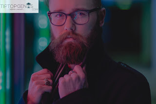 A man with lang beard, wearing a jacket and spects.