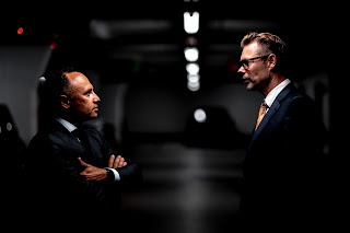 Two men in black suit talking with each other.